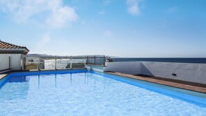 Ein Pool auf dem Dach mit klarem, blauem Wasser, Blick auf den Ozean und einen wolkenlosen Himmel.