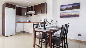 Eine moderne Küche mit dunklen Schränken, einem weißen Kühlschrank und einem Essbereich mit Tisch für zwei Personen.