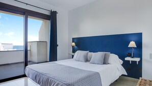 Habitación de hotel moderna con una cama grande, dos mesitas de noche con lámparas, vistas al mar y un balcón.