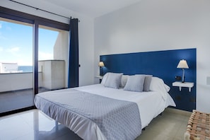 Een moderne hotelkamer met een groot bed, twee nachtkastjes met lampen, uitzicht op zee en een balkon.
