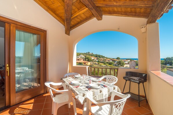 Un balcón con mesa lista para comer, una parrilla y vistas a un pueblo.