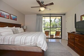 Un dormitorio con cama, ventilador de techo, televisión y vista a un jardín a través de una puerta corrediza.