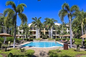 A hotel with a central swimming pool surrounded by palm trees and lounge chairs.