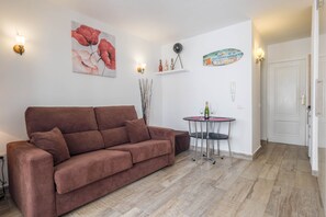 Una sala de estar con un sofá marrón, una mesita redonda con una botella y un vaso, y una puerta al fondo.