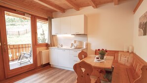 A wooden interior with a dining table, chairs, a kitchen area, and a sliding glass door leading to an outdoor patio. - Apartment "Toni - Obermösslhof" with Wi-Fi, Terrace & Mountain View (Lana)