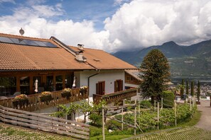 A traditional chalet with a sloped roof, wooden balcony, and a view of mountains and a lake.