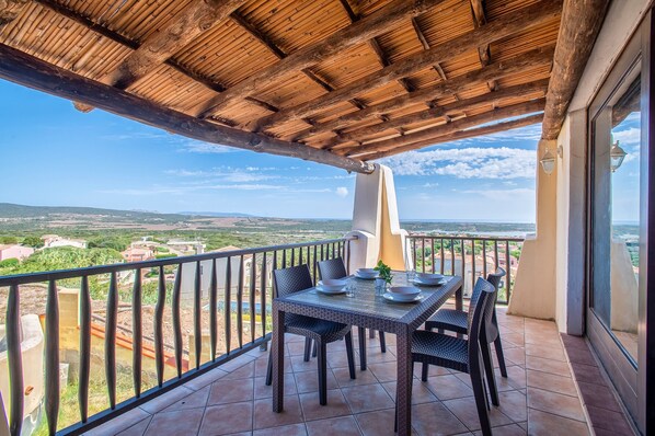 A balcony with a table set for dining, a view of the countryside, and a wooden ceiling. - Apartment "Corallo" with Fantastic Sea View and Balcony 090089-APR-00022 (Località Punta de Su Turrione, Stintino)