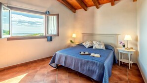 Ein Schlafzimmer mit Bett, Nachttisch, Fenster mit Blick und Holzboden.