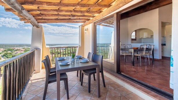 Ein Balkon mit Esstisch und Stühlen, Blick auf die Landschaft und Holzbalkendecke.