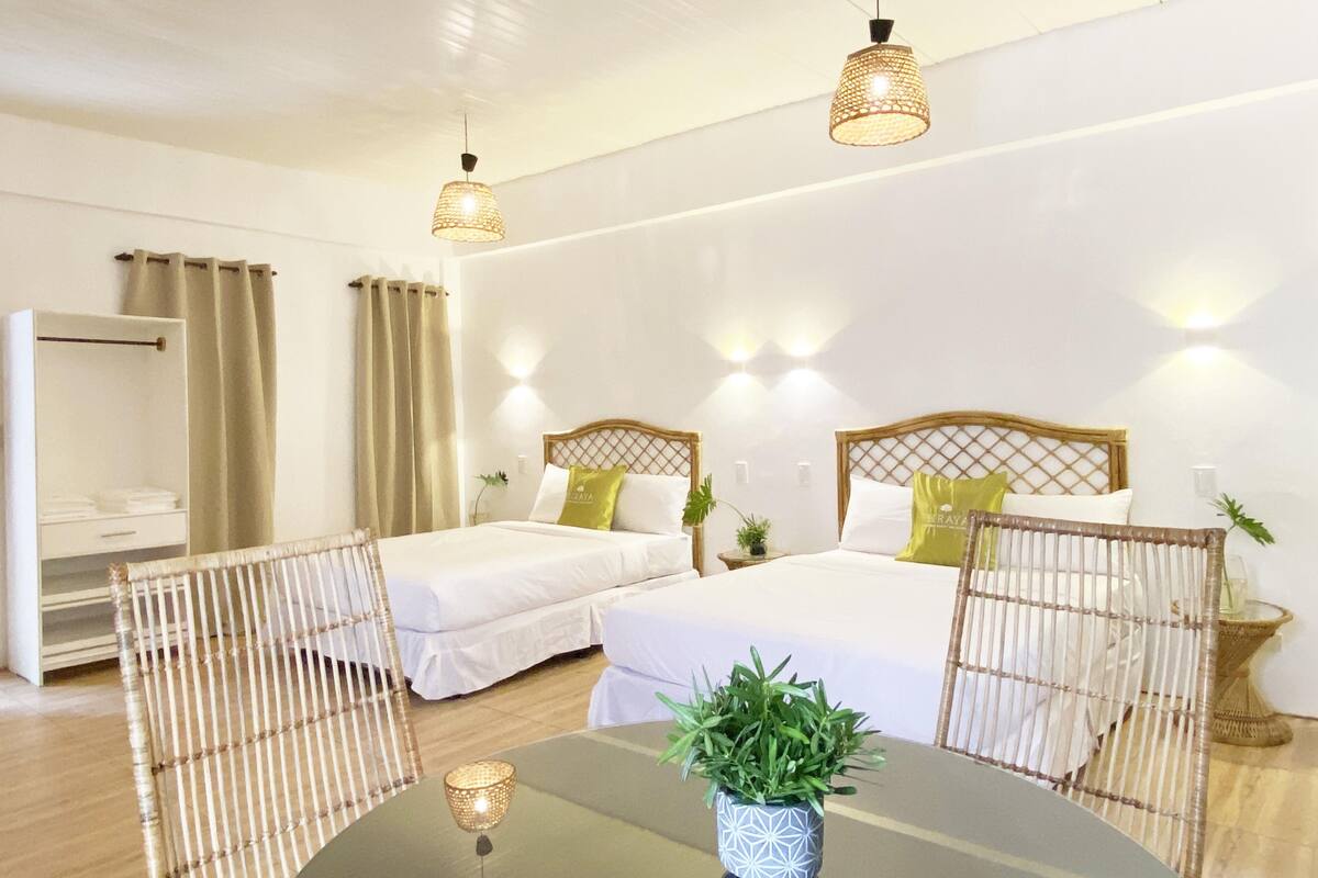 A hotel room with two single beds, a sitting area with a table, and a large window with curtains.
