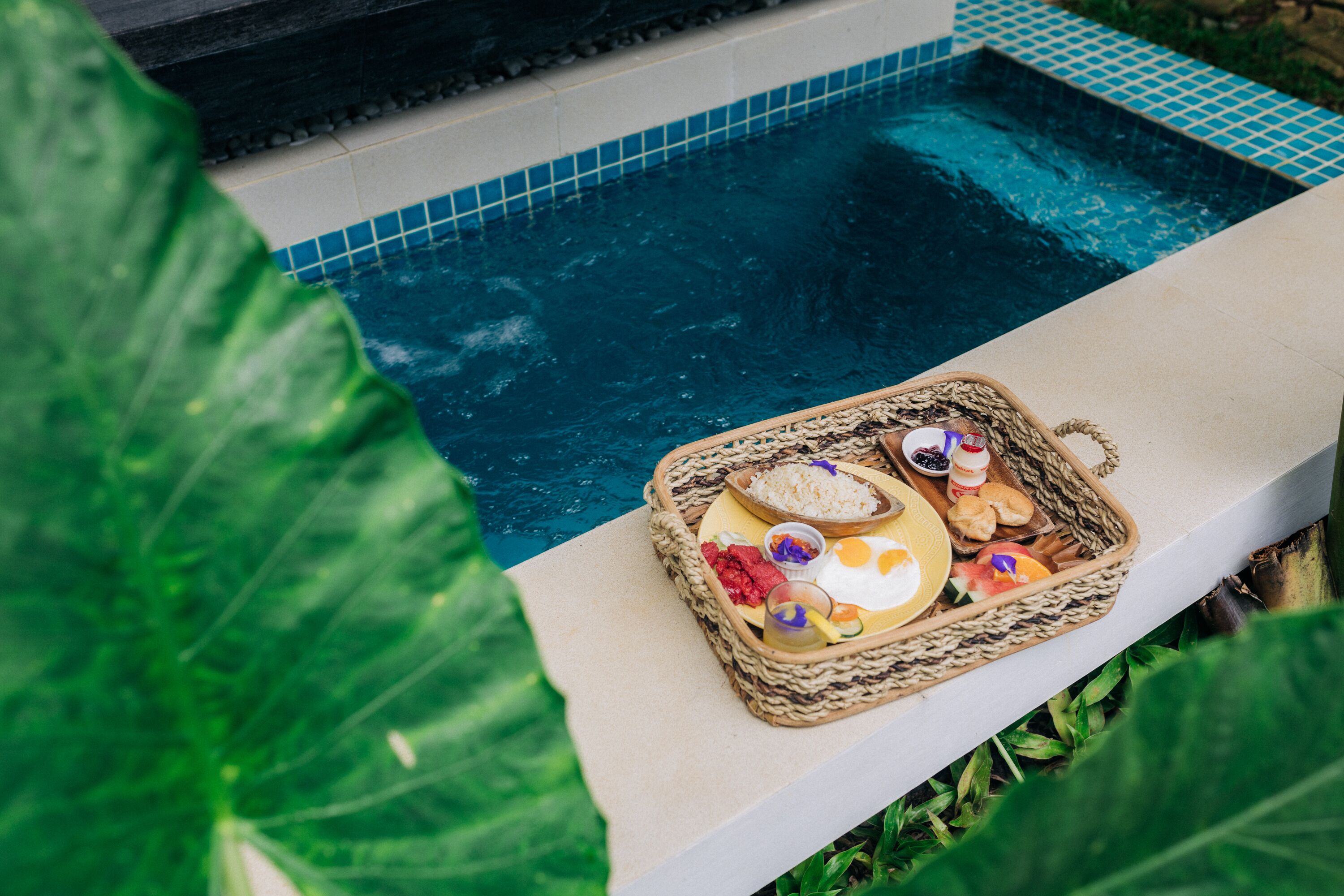 A poolside area with a wicker basket containing food items and a drink.