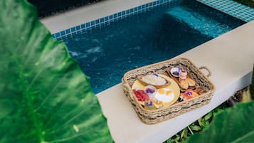 A poolside area with a wicker basket containing food items and a drink.