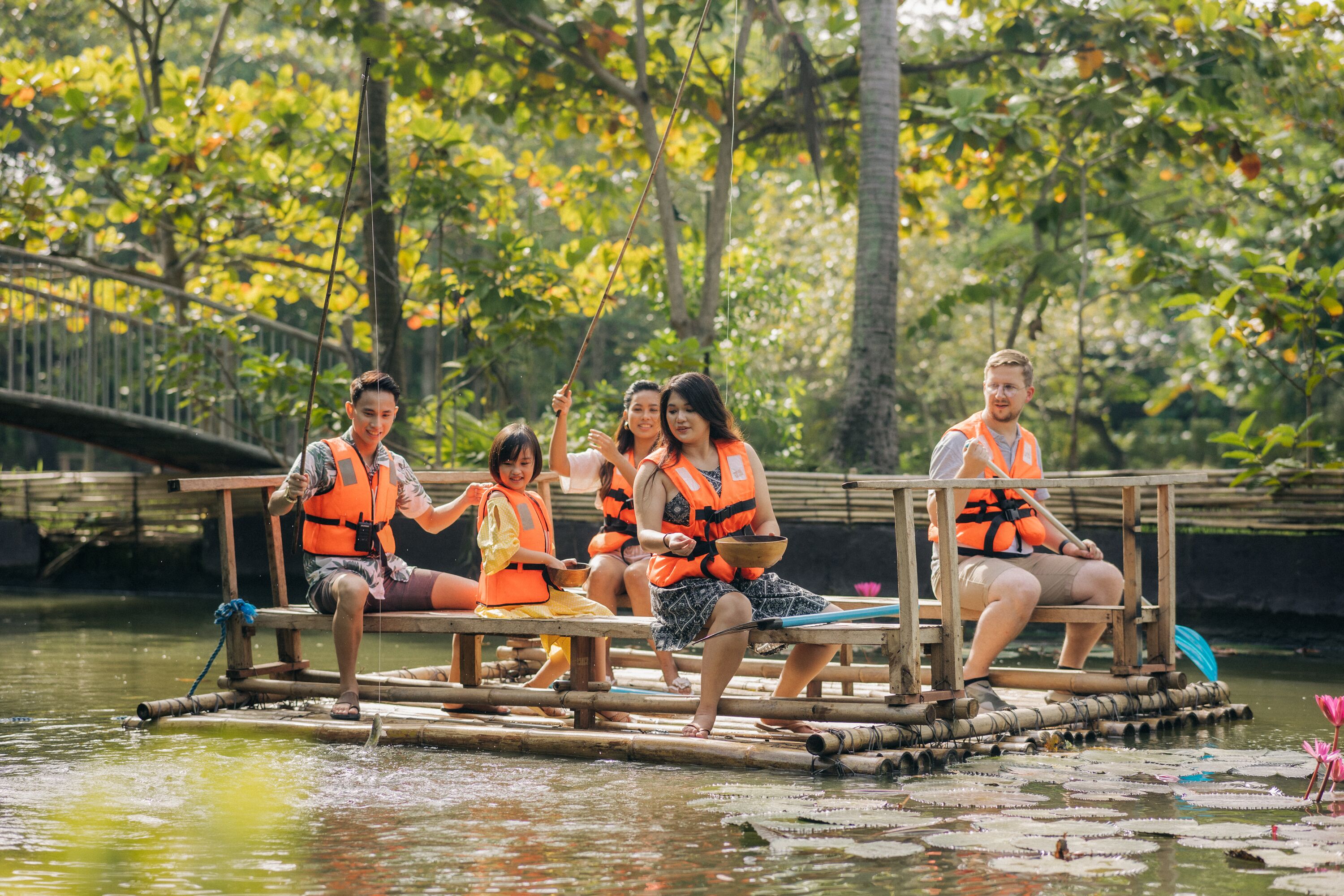 A group of people on a bamboo raft in a calm river surrounded by lush greenery.