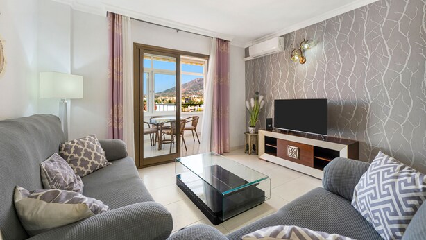 A modern living room with a sofa, a glass coffee table, a TV, and a balcony with a view. - Beautiful Adriana Apartment with Pool, Air Conditioning, Wi-Fi, Balcony, Terrace, Stunning Views (Fuengirola)