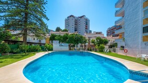 A swimming pool with a tiled edge, surrounded by a green lawn and trees. - Beautiful Adriana Apartment with Pool, Air Conditioning, Wi-Fi, Balcony, Terrace, Stunning Views (Fuengirola)