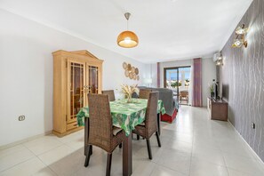 A dining area with a table set for four, surrounded by wicker chairs, a wooden cabinet, and a hanging light fixture. - Beautiful Adriana Apartment with Pool, Air Conditioning, Wi-Fi, Balcony, Terrace, Stunning Views (Fuengirola)