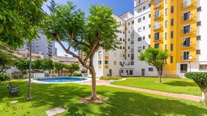 A residential building with a swimming pool, green lawns, and a tree in the foreground. - Beautiful Adriana Apartment with Pool, Air Conditioning, Wi-Fi, Balcony, Terrace, Stunning Views (Fuengirola)