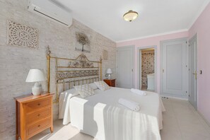 A bedroom with a large bed, a wooden nightstand, a wall-mounted air conditioner, and a door leading to another room. - Beautiful Adriana Apartment with Pool, Air Conditioning, Wi-Fi, Balcony, Terrace, Stunning Views (Fuengirola)