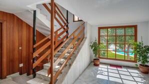 A staircase with wooden railings, a potted plant, and a view of a pool through a large window. - Beautiful Adriana Apartment with Pool, Air Conditioning, Wi-Fi, Balcony, Terrace, Stunning Views (Fuengirola)