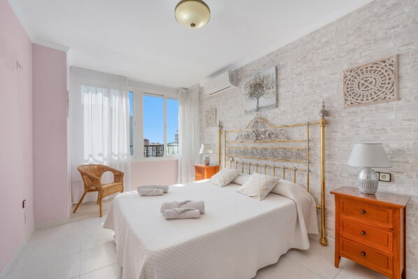 A bedroom with a bed, a chair, a nightstand, and a window with curtains. - Beautiful Adriana Apartment with Pool, Air Conditioning, Wi-Fi, Balcony, Terrace, Stunning Views (Fuengirola)