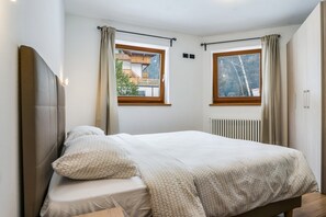 A bedroom with a bed, two windows, a radiator, and a curtain rod.