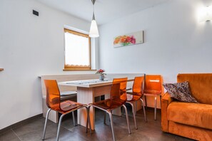 A modern kitchen with a dining area, featuring a wooden table, orange chairs, and a sofa with a leopard print pillow.