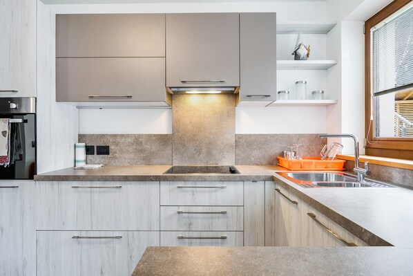 A modern kitchen with a built-in oven, a stainless steel sink, and a window with blinds.