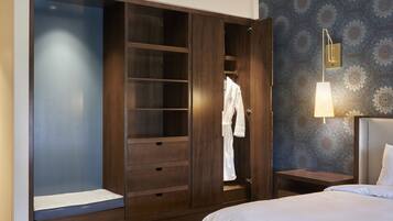 A hotel room with a large walk-in closet, a bed, a nightstand, and a wall-mounted lamp.