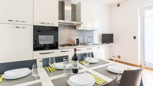 Une cuisine moderne avec des meubles blancs, un four encastré et un coin repas avec une table dressée pour deux personnes.