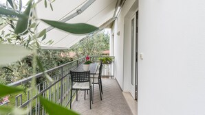 Un balcon avec une table et des chaises, un pot de fleurs et une vue sur la verdure.