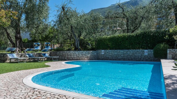 Une piscine bordée de pierres, des chaises longues et un mur de pierre sur lequel est apposée une pancarte indiquant l’interdiction d’accès.