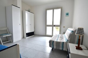 A room with a bed, a chair, a wardrobe, a lamp, and a window.