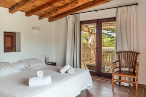 Een slaapkamer met een bed, een stoel, een nachtkastje en een deur naar een buitenruimte.