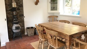 A dining area with a stone wall, a wooden table, and chairs. - Small cottage with wonderful sea view from the terrace,  sleeps 2 to 4 adults (15 miles to Swansea)