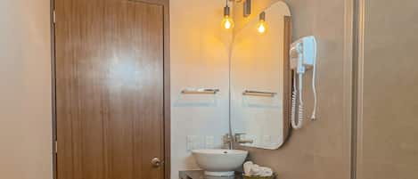 A bathroom with a wooden door, a white toilet, a sink with a mirror above it, and two wall-mounted light fixtures.