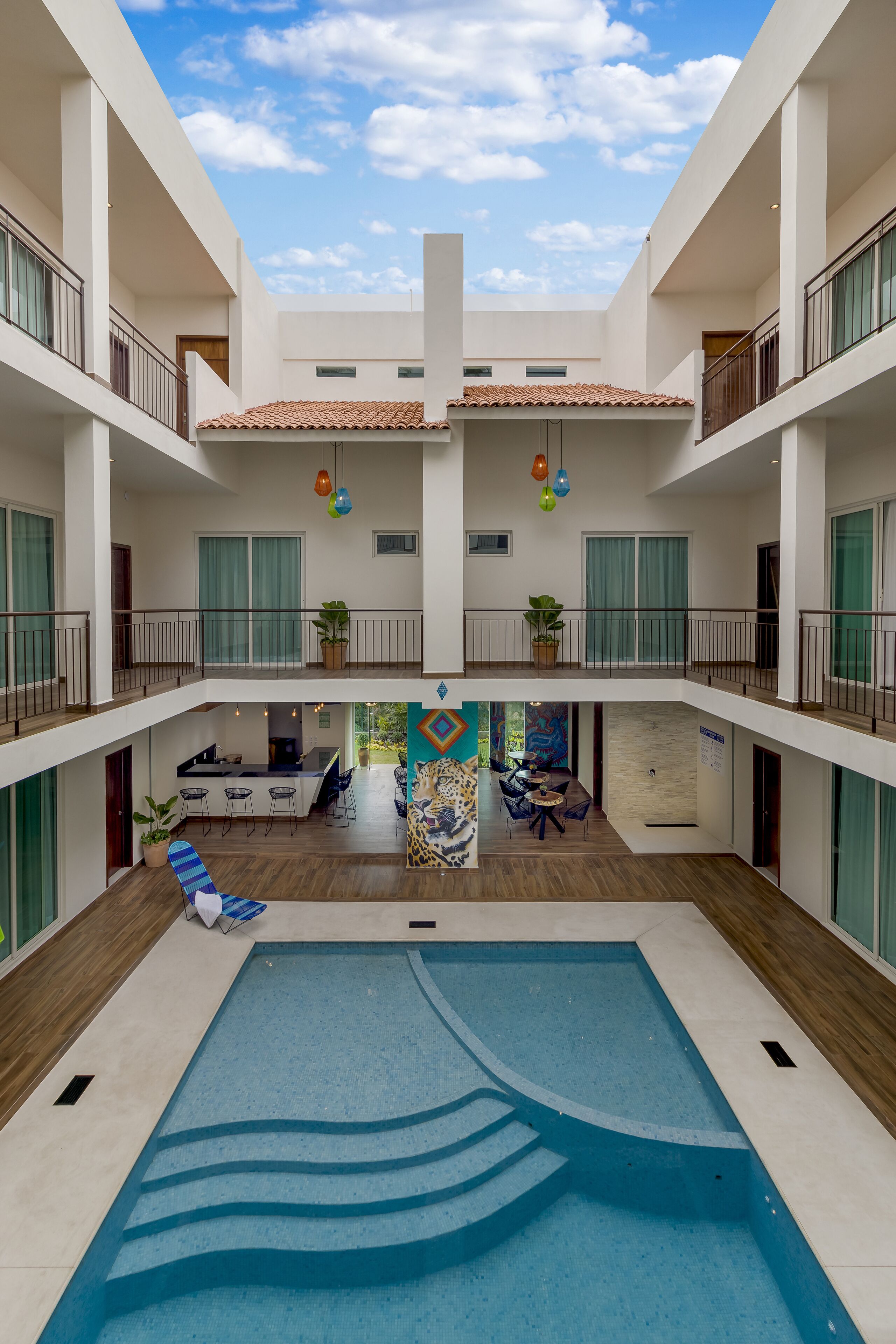 A multi-level indoor pool area with a central pool, multiple balconies, and a dining area with outdoor seating.