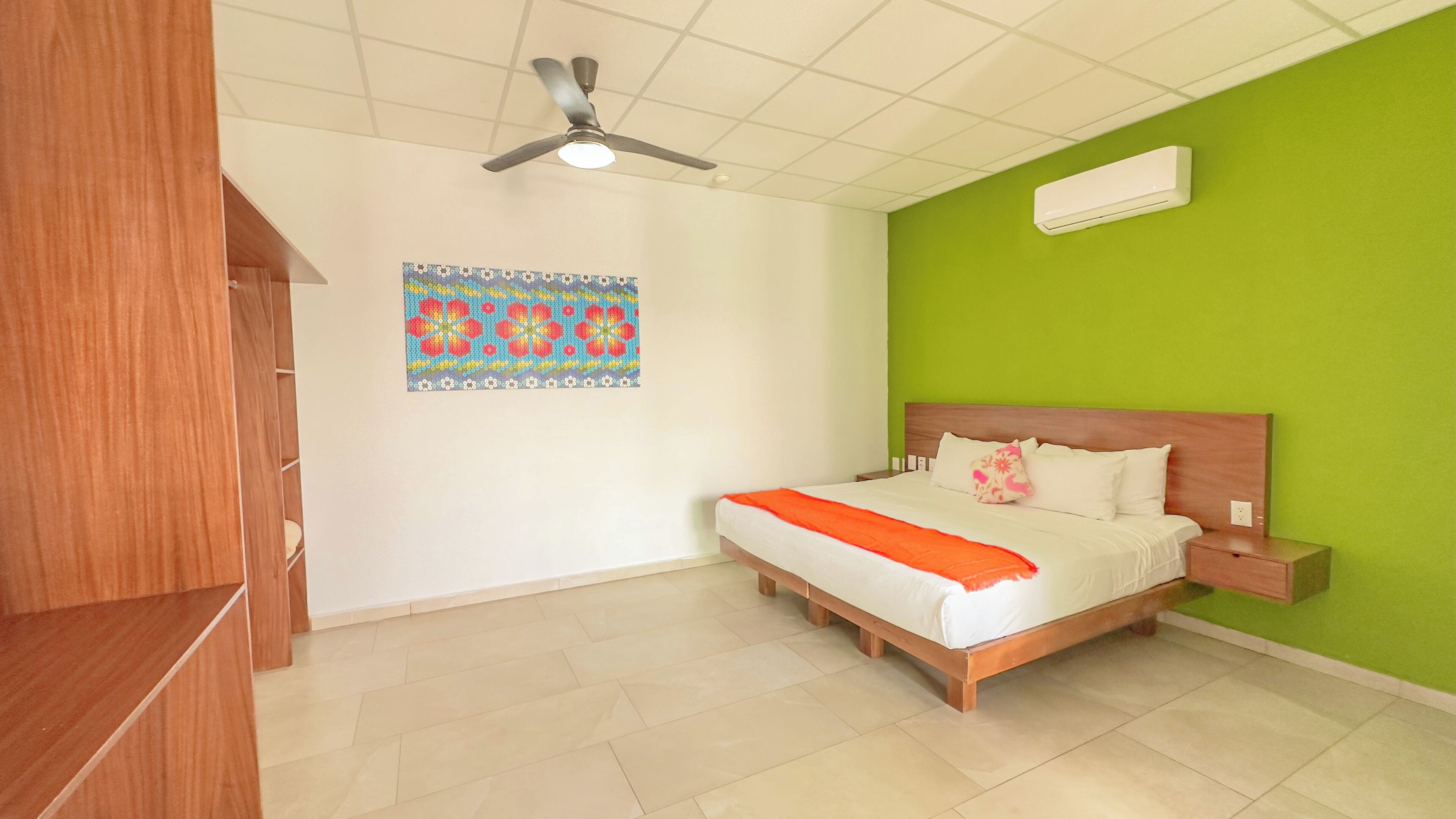 Une chambre à coucher avec un lit, un ventilateur de plafond, un climatiseur fixé au mur et une décoration murale colorée.