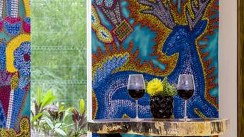 A table with two glasses of red wine and a vase with yellow flowers against a colorful tapestry backdrop.