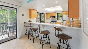 Een moderne keuken met witte kasten, een bar met krukken en uitzicht op de omgeving.