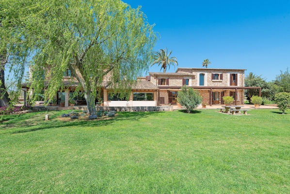 A two-story house with a patio, a lawn, and a tree.