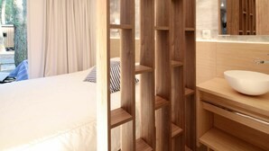 Ein modernes Hotelzimmer mit einem Bett, einer Holzauslage, einem Badezimmer mit Waschbecken und einem großen Fenster mit Vorhängen.