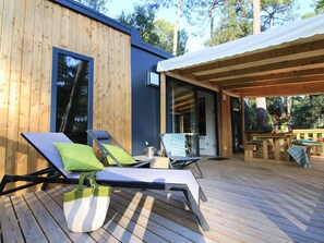 A wooden deck with two sun loungers, a table, and a covered area.