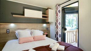 Een slaapkamer met een bed, kussens, een bruine deken, een witte handdoek, een houten hoofdbord, een plank boven het bed en uitzicht op een balkon met een hekwerk.