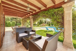 Un patio al aire libre con mobiliario de mimbre, una piscina y follaje.