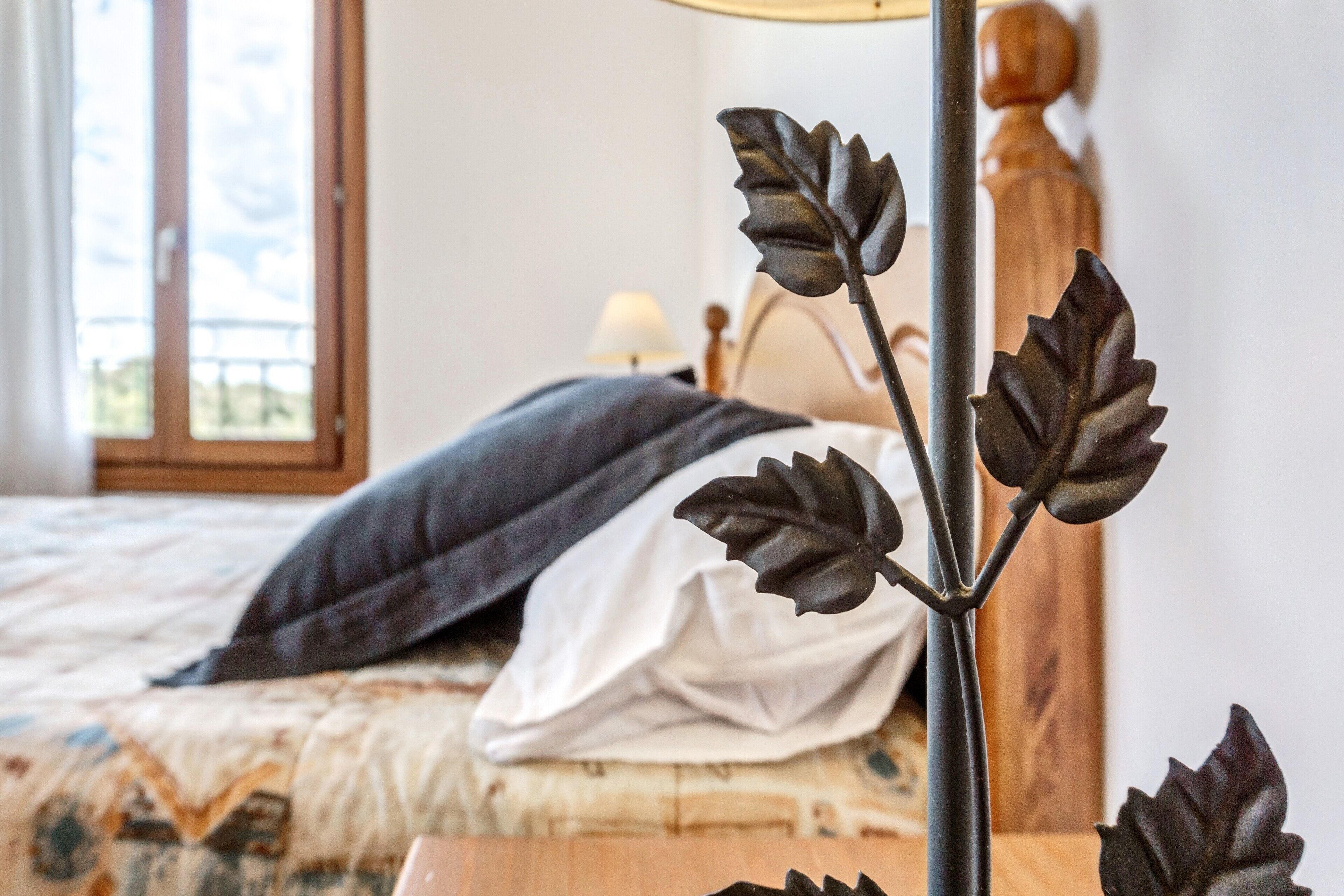 A bed with a dark pillow and a white pillow, a wooden headboard, and a window with a view of greenery.