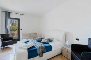 Een slaapkamer met een bed, een stoel, een nachtkastje en een raam.