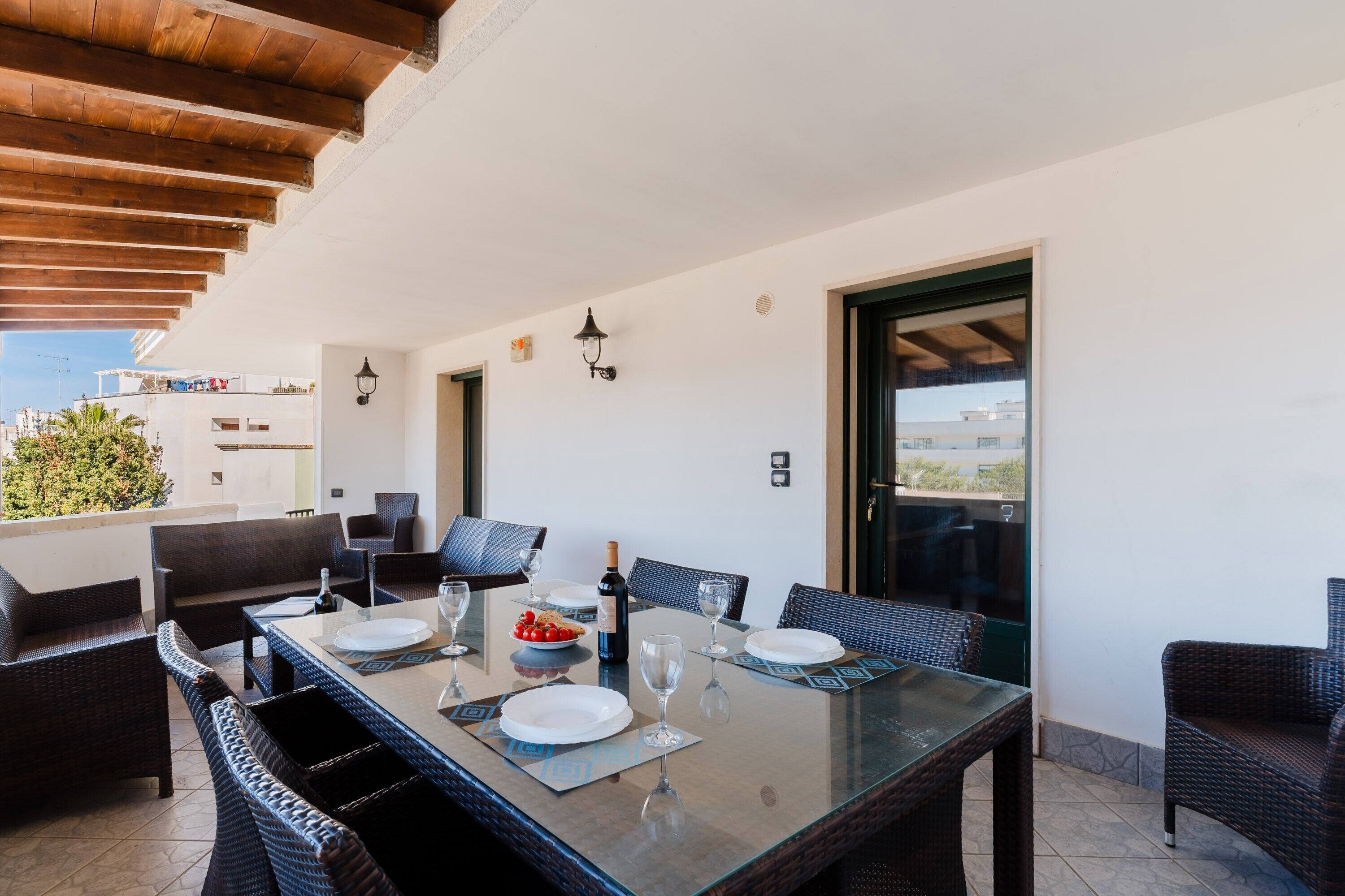Un espacio exterior para comer con mobiliario de mimbre, una mesa de vidrio y vistas a la ciudad.