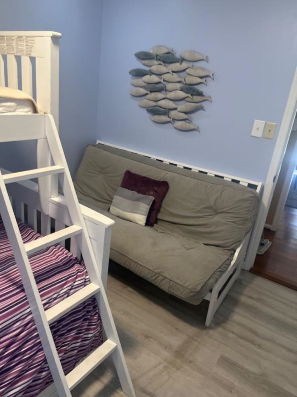 Un lit superposé avec un matelas à rayures, un canapé beige avec un coussin et une décoration murale représentant des poissons.