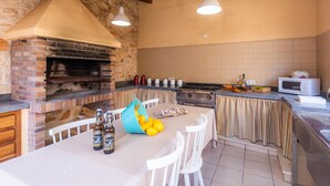 A kitchen with a brick oven, white chairs, a table with bottles, and a microwave. - Holiday Home Casa Hermosa with Pool, Terrace, Air Conditioning and WiFi (Capdepera)