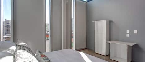 A modern hotel room with a large bed, a wardrobe, and a desk.